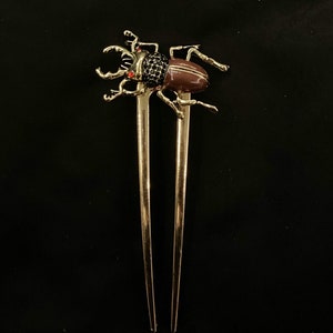 May include: Gold hair stick with a decorative beetle design. The beetle is black and brown with red accents.