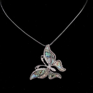 May include: A butterfly pendant necklace with iridescent abalone shell wings and a silver-tone metal frame. The butterfly has a small diamond accent in the center and is suspended from a thin black cord. The background is black.