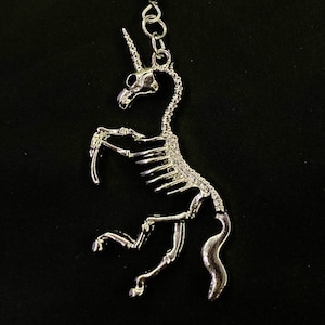 May include: A silver skeleton unicorn keychain with a detailed design. The unicorn is standing on its hind legs with its head tilted back.