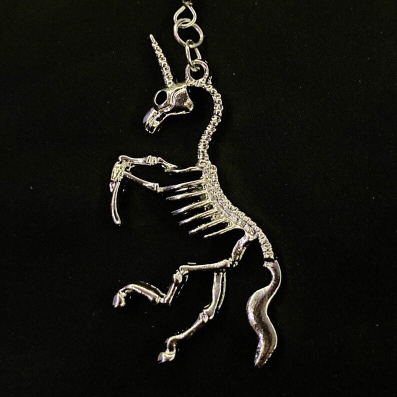 May include: A silver skeleton unicorn keychain with a detailed design. The unicorn is standing on its hind legs with its head tilted back.