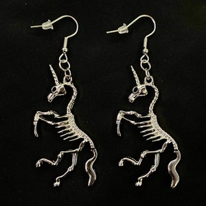 May include: A pair of silver skeleton unicorn earrings. The earrings are dangling and have a hook closure.