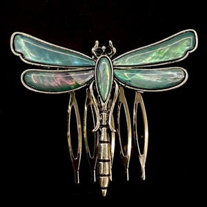 Könnte beinhalten: Ein silberner Libellen-Haarkamm mit schillernden grünen Flügeln. Der Kamm hat fünf Zinken.