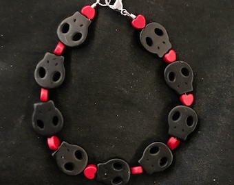 May include: A black and red skull and heart charm bracelet. The bracelet is made of black plastic beads with a skull design and red plastic beads with a heart design. The bracelet has a silver clasp.