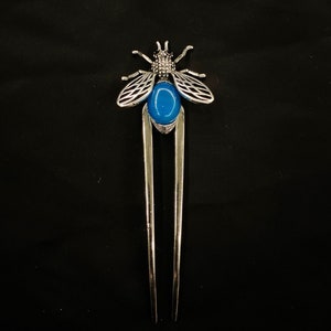 May include: Silver hair fork with a blue gemstone in the centre and a decorative silver bee design.
