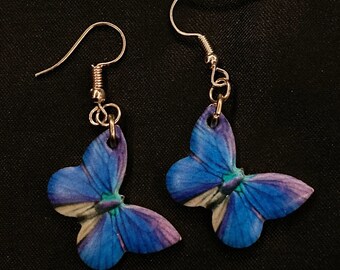 May include: A pair of dangle earrings featuring blue butterfly charms with silver hooks.