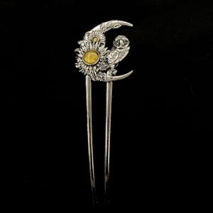 Può includere: Fermaglio per capelli argentato con design a mezzaluna, girasole e gufo. Il girasole ha un centro in pietra preziosa gialla. Il gufo è appollaiato sulla luna. Due lunghi perni paralleli si estendono dalla parte superiore decorativa. Lo sfondo è nero.