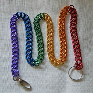 Puede incluir: Una cadena de colores arcoíris con un llavero plateado adjunto. La cadena está hecha de pequeños anillos de metal y mide aproximadamente 45 cm de largo.