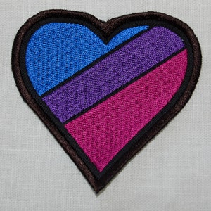 May include: A heart-shaped embroidered patch with a black outline and three stripes of blue, purple, and pink.