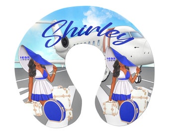 May include: A white travel neck pillow with a blue and white illustration of a woman in a blue hat and dress, holding luggage, walking on a runway in front of a private jet. The text "Shirley" is written in a cursive font on the pillow.