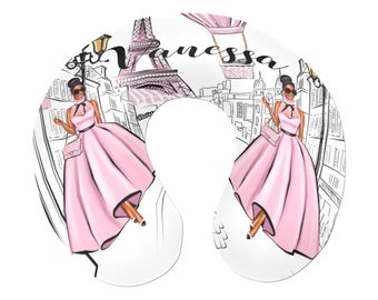 May include: A white travel neck pillow with a black and white illustration of the Eiffel Tower, a hot air balloon, and a woman in a pink dress. The text "Vanessa" is written across the top of the pillow.