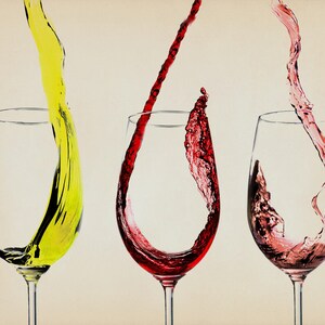 May include: Three wine glasses with different colored liquids pouring into them. The glass on the left has a yellow liquid, the middle glass has a red liquid, and the glass on the right has a pink liquid.