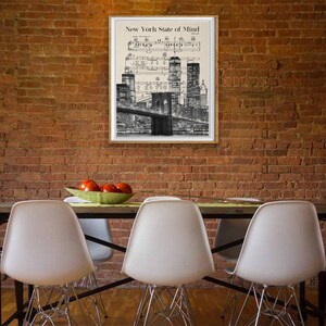 May include: A black and white print of the New York City skyline with the Brooklyn Bridge in the foreground. The print is framed and hanging on a brick wall. The text "New York State of Mind" is printed at the top of the print.