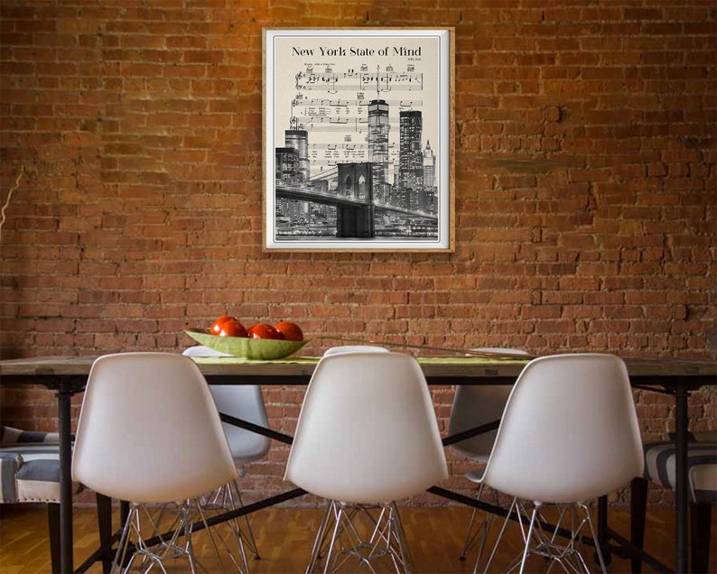 May include: A black and white print of the New York City skyline with the Brooklyn Bridge in the foreground. The print is framed and hanging on a brick wall. The text "New York State of Mind" is printed at the top of the print.