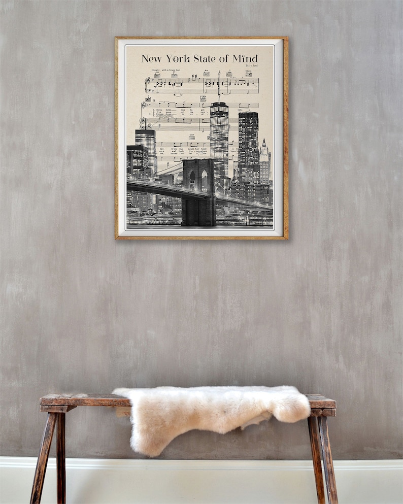 May include: A black and white print of the New York City skyline with the Brooklyn Bridge in the foreground. The print is framed in a wooden frame and has the song title "New York State of Mind" and the songwriter's name "Billy Joel" printed at the top.