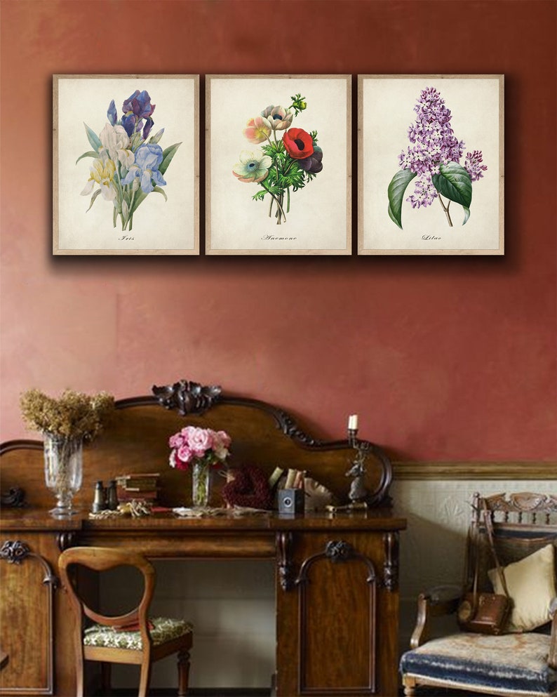 May include: Three vintage botanical prints framed in a simple white frame. The prints feature a blue iris, a red and white anemone, and a purple lilac. The prints are labeled "Iris", "Anemone", and "Lilac".