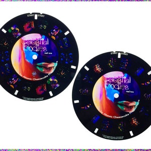 Könnte beinhalten: Zwei schwarze kreisförmige Scheiben mit bunten Bildern und Text. Der Text auf den Scheiben lautet "Celestial Bodies" und "real one" und "real two". Der Text "for Atomic Cheesecake Productions" befindet sich ebenfalls auf den Scheiben.