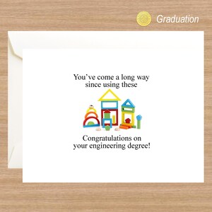 May include: A graduation card with a humorous message about building blocks and an engineering degree. The card features a colorful illustration of wooden building blocks arranged to look like houses.