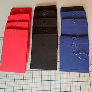 May include: Three stacks of envelopes, each in a different color: red, black, and blue. Each envelope has a button closure.