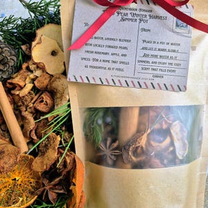Könnte beinhalten: Ein klarer Beutel mit getrockneten Birnen, Rosmarin, Apfel und Gewürzen. Ein Etikett mit rotem Band trägt die Aufschrift "Pear Winter Harvest Simmer Pot" und Anweisungen. Der Beutel ist von getrockneten Früchten und Grün umgeben.