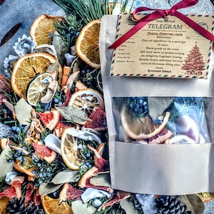 Könnte beinhalten: Ein festliches Arrangement aus getrockneten Zitrusfrüchten, Kiefernzweigen und Wacholderbeeren. Ein klarer Beutel enthält ähnliche Zutaten. Ein mit rotem Band gebundenes Etikett trägt die Aufschrift "Coastal Christmas Cheer" mit Anweisungen.