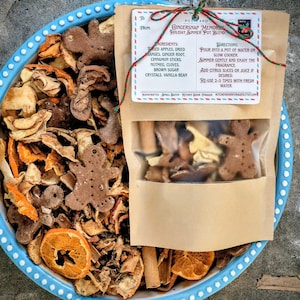 Puede incluir: Un cuenco de cerámica azul y blanco lleno de fruta deshidratada, hombres de jengibre y una bolsa de papel kraft que contiene una mezcla para olla a fuego lento. La bolsa tiene una ventana transparente y una etiqueta que dice "Gingersnap Memories".