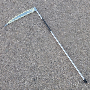 May include: A silver scythe with a black handle. The blade is curved and has a serrated edge.