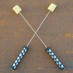 May include: Two silver fire poi with black handles. The handles have a geometric pattern with silver accents. The poi are crossed in an X shape.