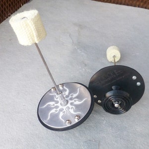 May include: Two fire spinning poi with black and silver bases. One base has a tribal design and the other has the text "Fire Tricks Concepts" on it. Both poi have white wick material attached to the end of the spinning cable.