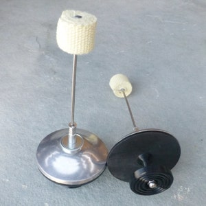 May include: Two fire poi with black and silver bases and white wick tips. The poi are on a gray surface.