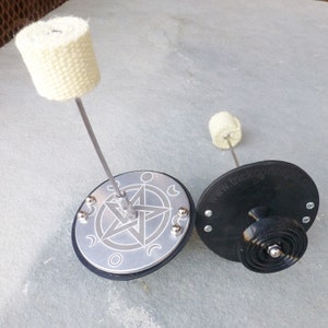 May include: Two fire spinning poi with black bases and white wick. The base on the left has a silver pentagram design with moons around it. The base on the right has the text "www.trick-concepts.de".