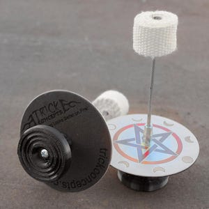 May include: Two fire spinning poi with a black and silver base. The base has the text "Trick Concepts" and "Looks Better on Fire!" The poi have a white wick and a silver metal rod.