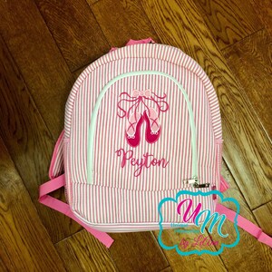 May include: Pink and white striped backpack with a pink embroidered ballerina shoe design and the name Peyton.
