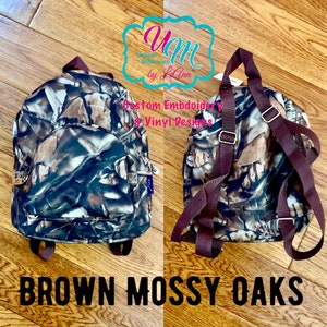 May include: A small brown and green camouflage backpack with brown straps. The backpack has a large pocket on the front and a smaller pocket on the side. The text "BROWN MOSSY OAKS" is printed below the backpack.