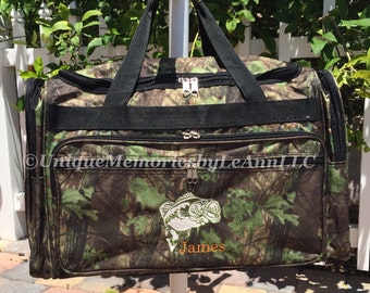 May include: A camouflage green and brown duffel bag with a black zipper and handles. The bag has an embroidered white bass fish and the name "James" in orange.
