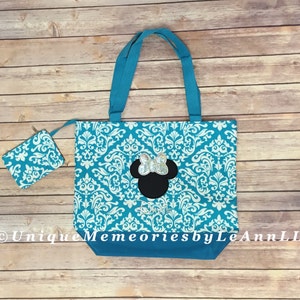 May include: A turquoise tote bag with a white damask pattern and a black Minnie Mouse silhouette with a silver glitter bow. The bag comes with a matching turquoise and white damask zippered pouch.