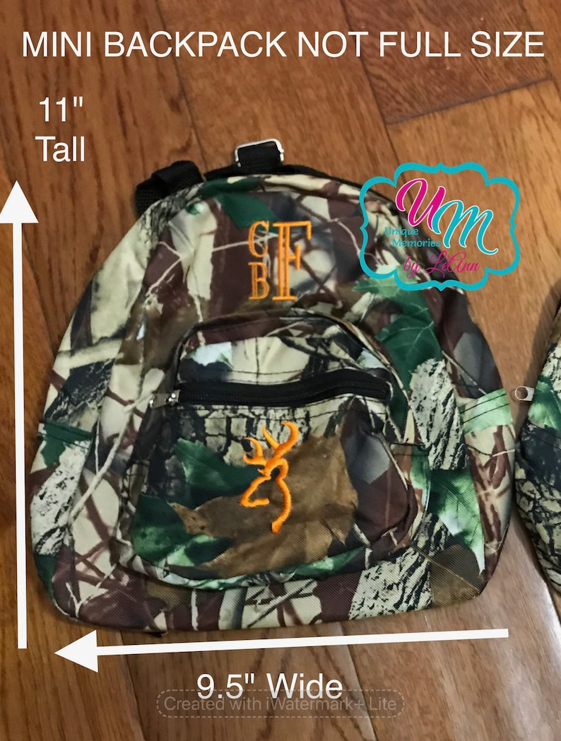 May include: A camouflage-patterned mini backpack with a black zipper and a brown and orange embroidered deer logo. The backpack is 11 inches tall and 9.5 inches wide.