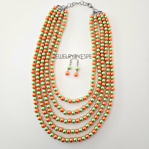 May include: A multi-strand necklace and matching earrings set featuring alternating green and orange faux pearls. The necklace is made of five strands of pearls and has a silver clasp. The earrings are silver with a single green pearl on each.