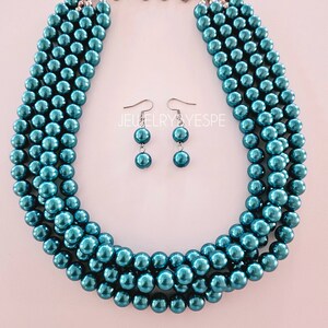 May include: A teal blue pearl necklace and matching earrings. The necklace is made of multiple strands of pearls and has a silver clasp. The earrings are simple and dangle.