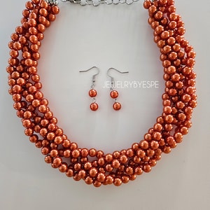 May include: A set of orange faux pearl jewelry featuring a multi-strand necklace and matching earrings. The necklace has a silver clasp and the earrings have silver hooks.