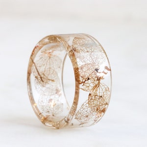 May include: A clear resin ring with dried leaves embedded inside. The ring is a light brown colour and has a smooth, polished finish.