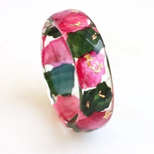 May include: A clear resin bangle bracelet with pink and green pressed flowers and gold leaf accents.