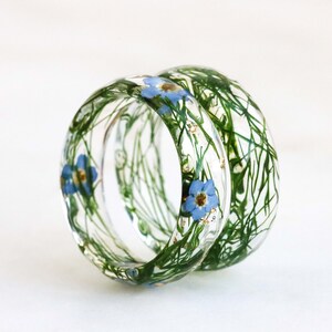May include: Two clear resin rings with embedded green foliage and blue flowers.
