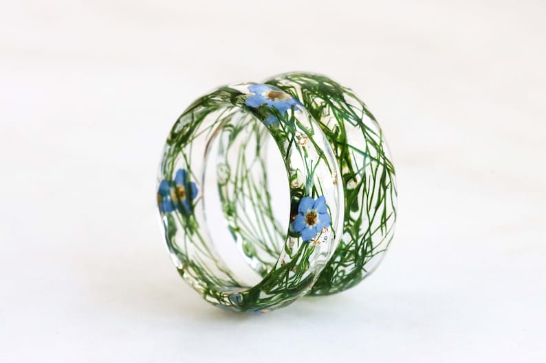 May include: Two clear resin rings with embedded green foliage and blue flowers.