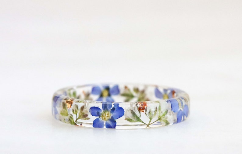 May include: A clear resin ring with embedded blue and white flowers and gold flecks.