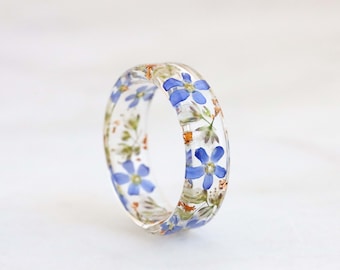May include: A clear resin ring with embedded blue flowers and green leaves.