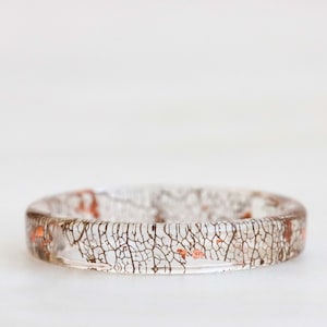 Könnte beinhalten: Ein transparenter Harzring mit einem zarten, braunen, baumrindenartigen Muster und Kupferflocken.