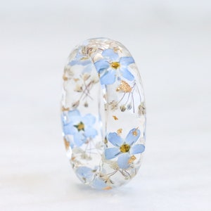 Faceted resin ring with real tiny blue forget-me-not, baby's breath flowers and gold, silver or copper flakes inside. The flowers are arranged one after another in a circle.