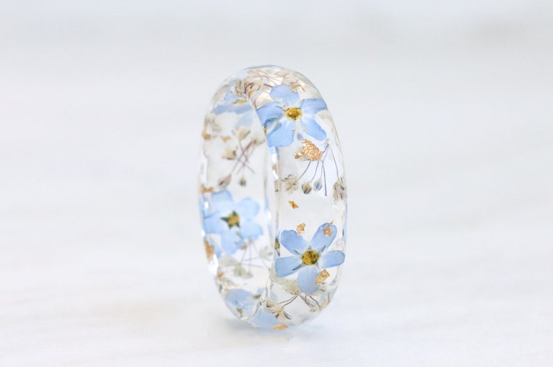 Faceted resin ring with real tiny blue forget-me-not, baby's breath flowers and gold, silver or copper flakes inside. The flowers are arranged one after another in a circle.