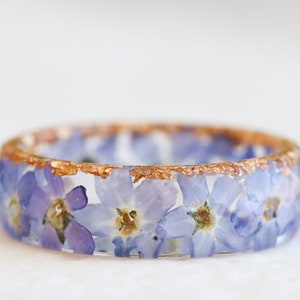 Faceted resin ring that contains real pressed blue purple forget-me-not flowers and gold, silver or copper flakes on the one side of the ring. The flowers are arranged in a circle, one after another and looks like a wreath.