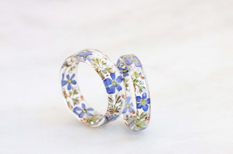 May include: Two clear resin rings with embedded blue and white flowers. The rings are stacked on top of each other.